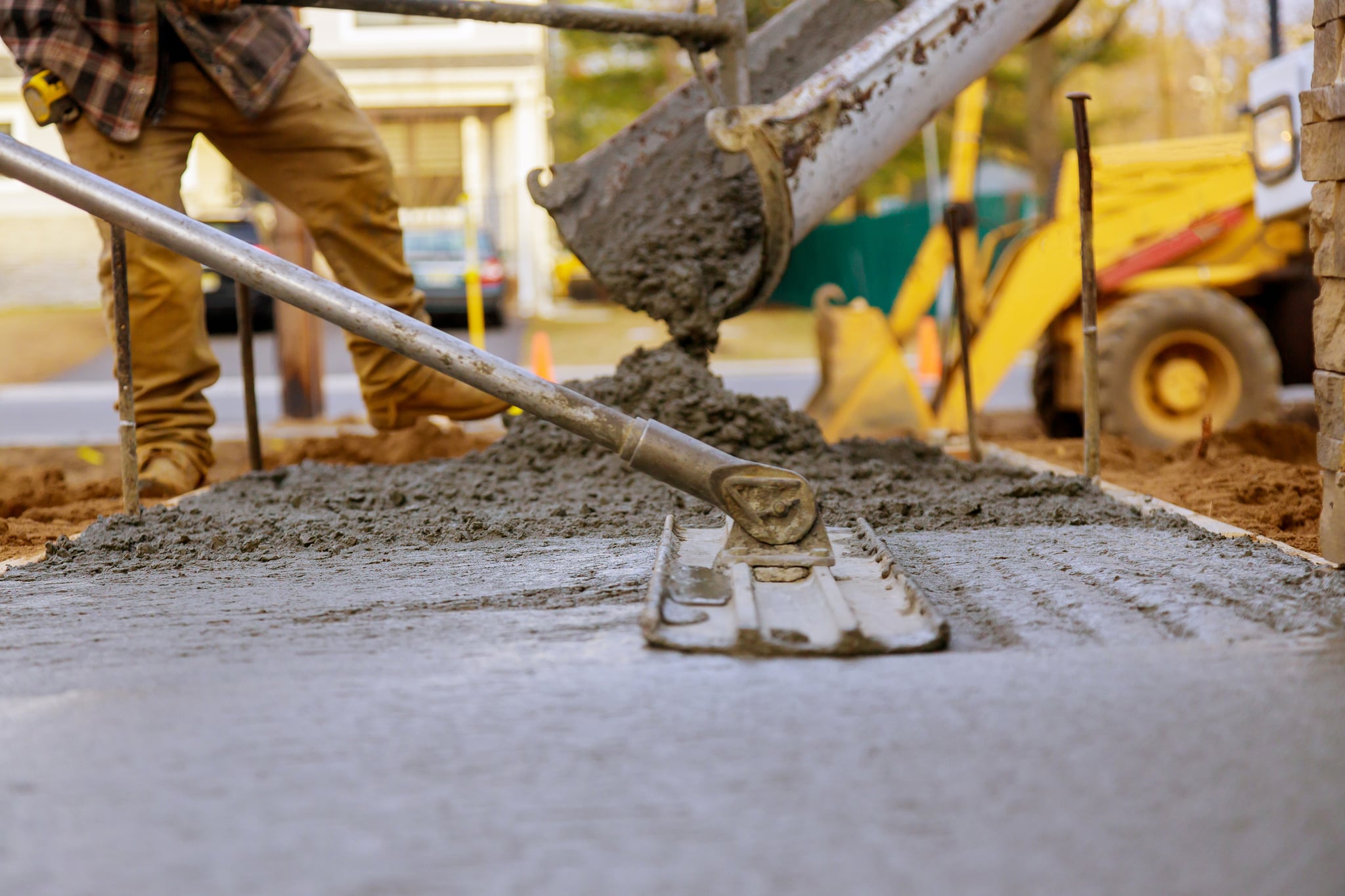 Worker smooths freshly poured concrete beside a backhoe.