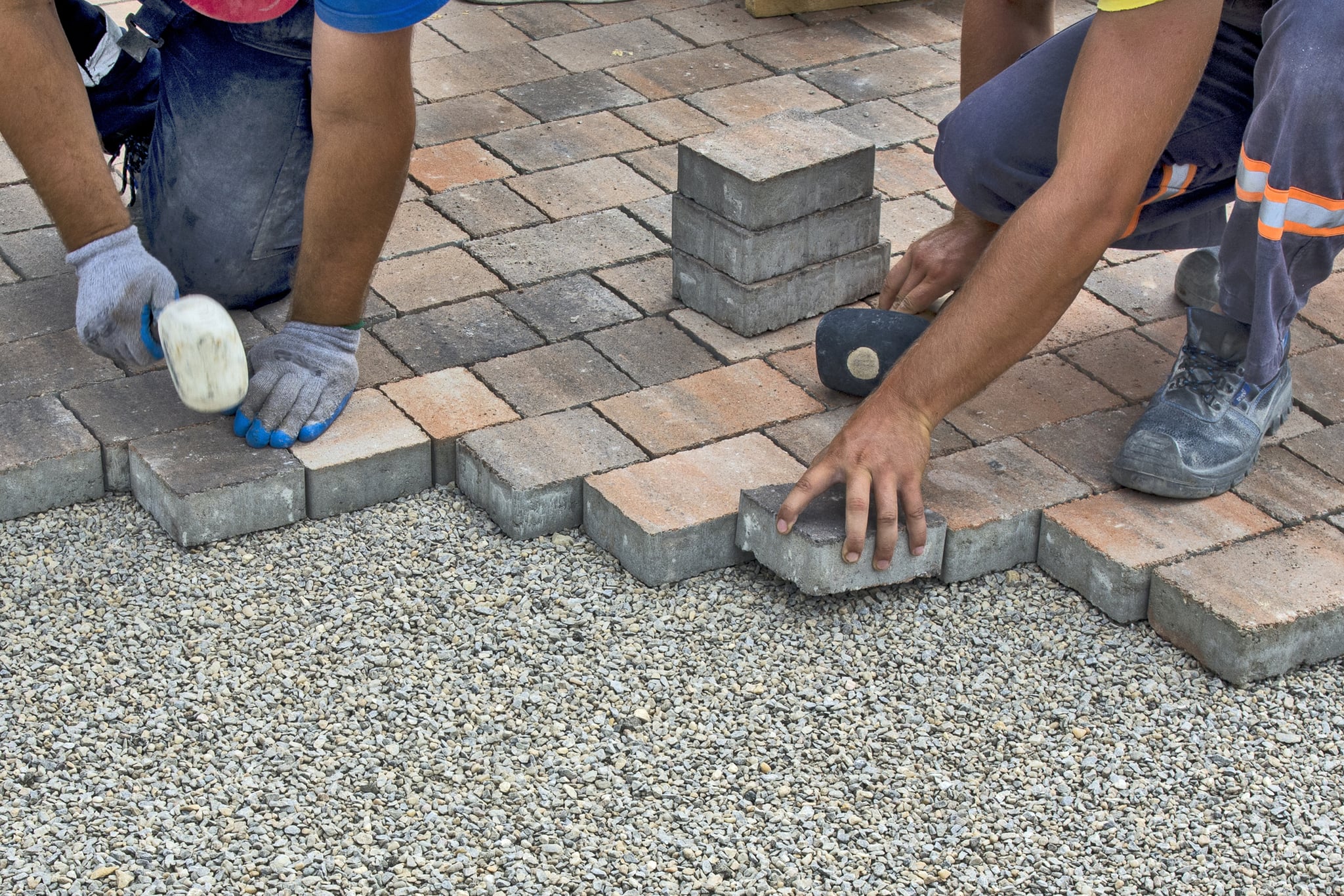 Workers installing interlocking pavers over a gravel base
