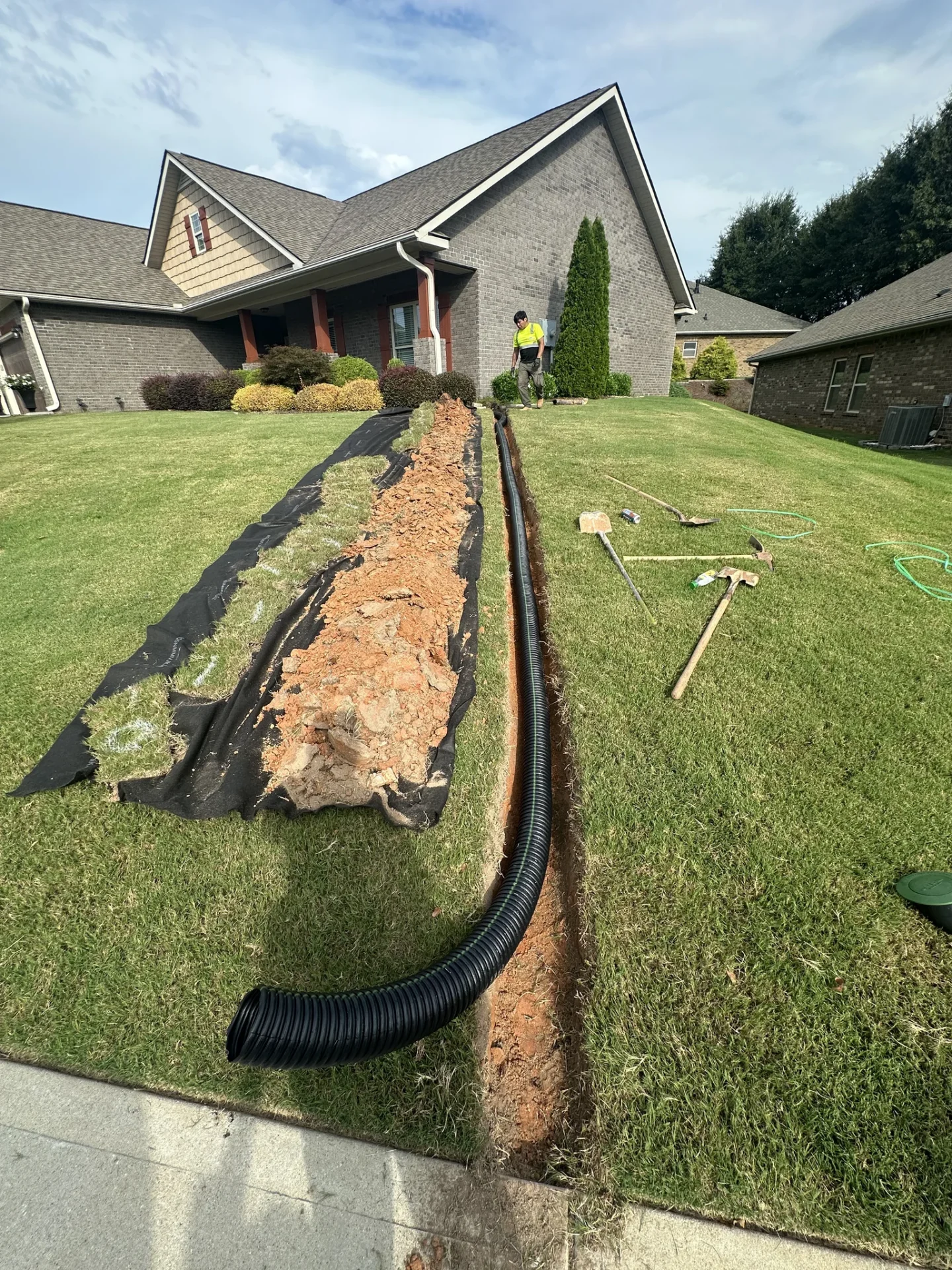 Worker installs drainage pipe beside suburban brick house