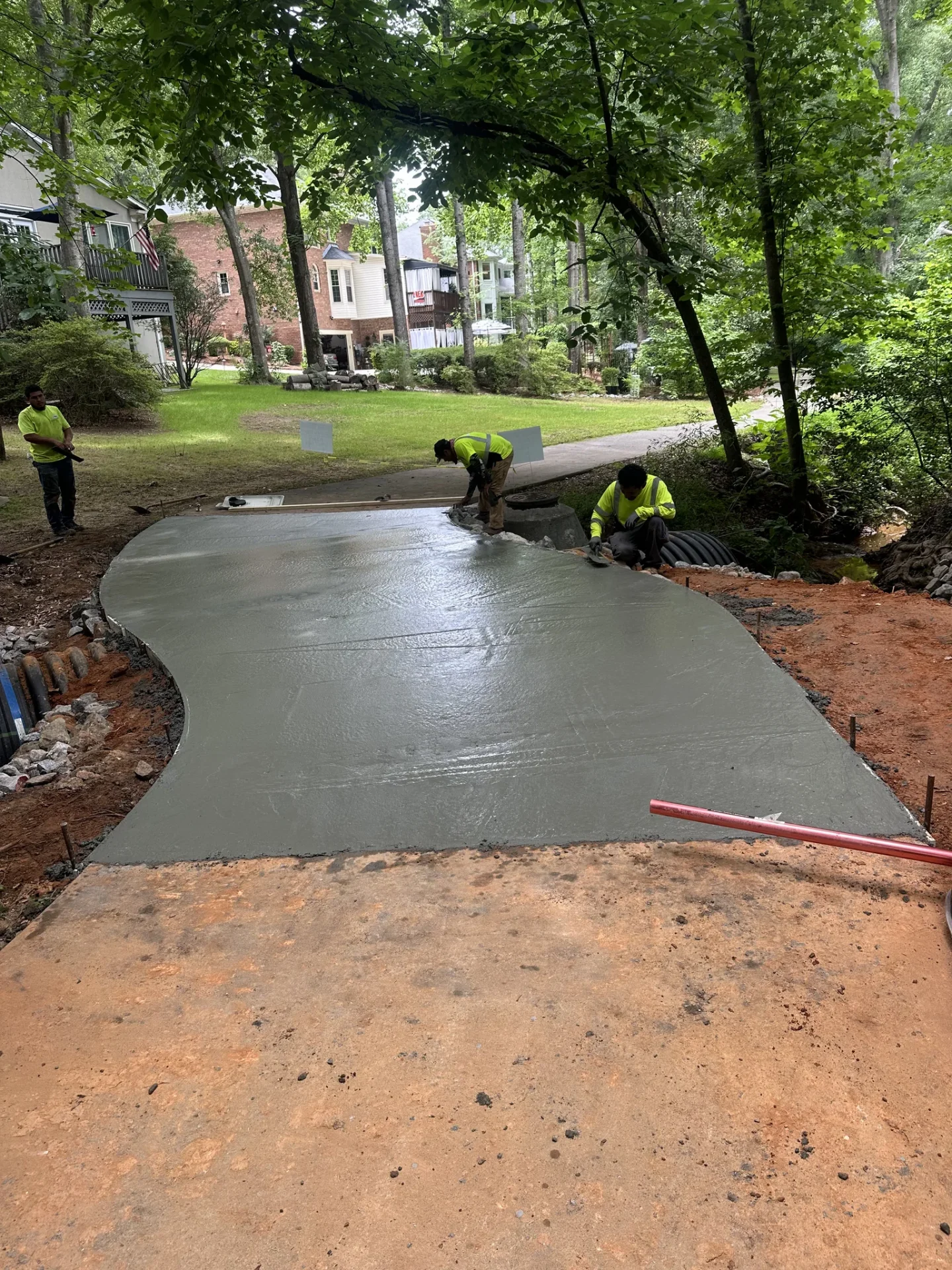 Workers finish new concrete path beside wooded neighborhood creek