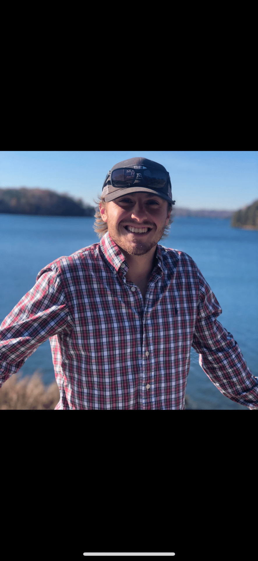 Smiling man in plaid shirt standing beside a lake
