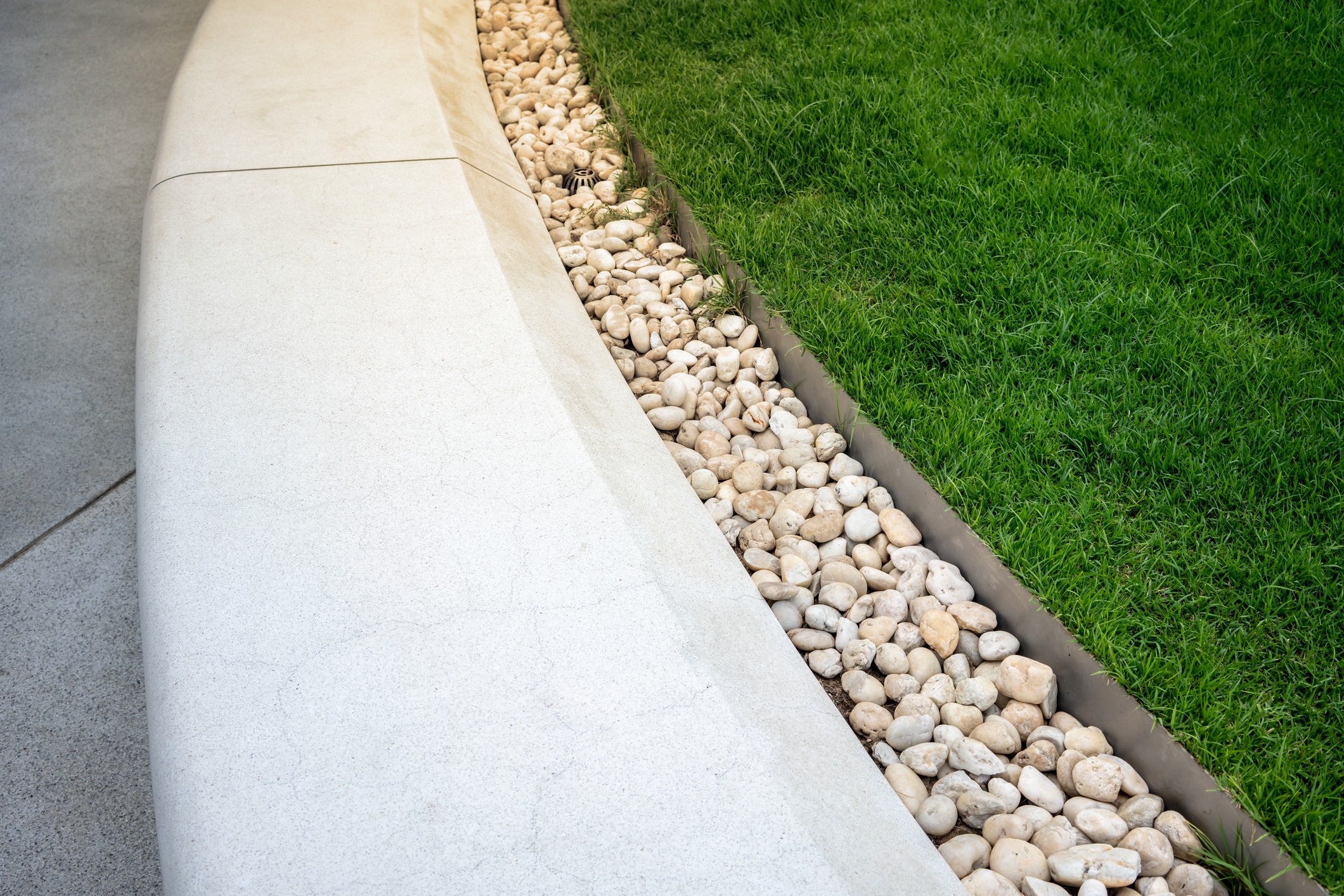 Rock-lined drainage channel beside sidewalk and green lawn
