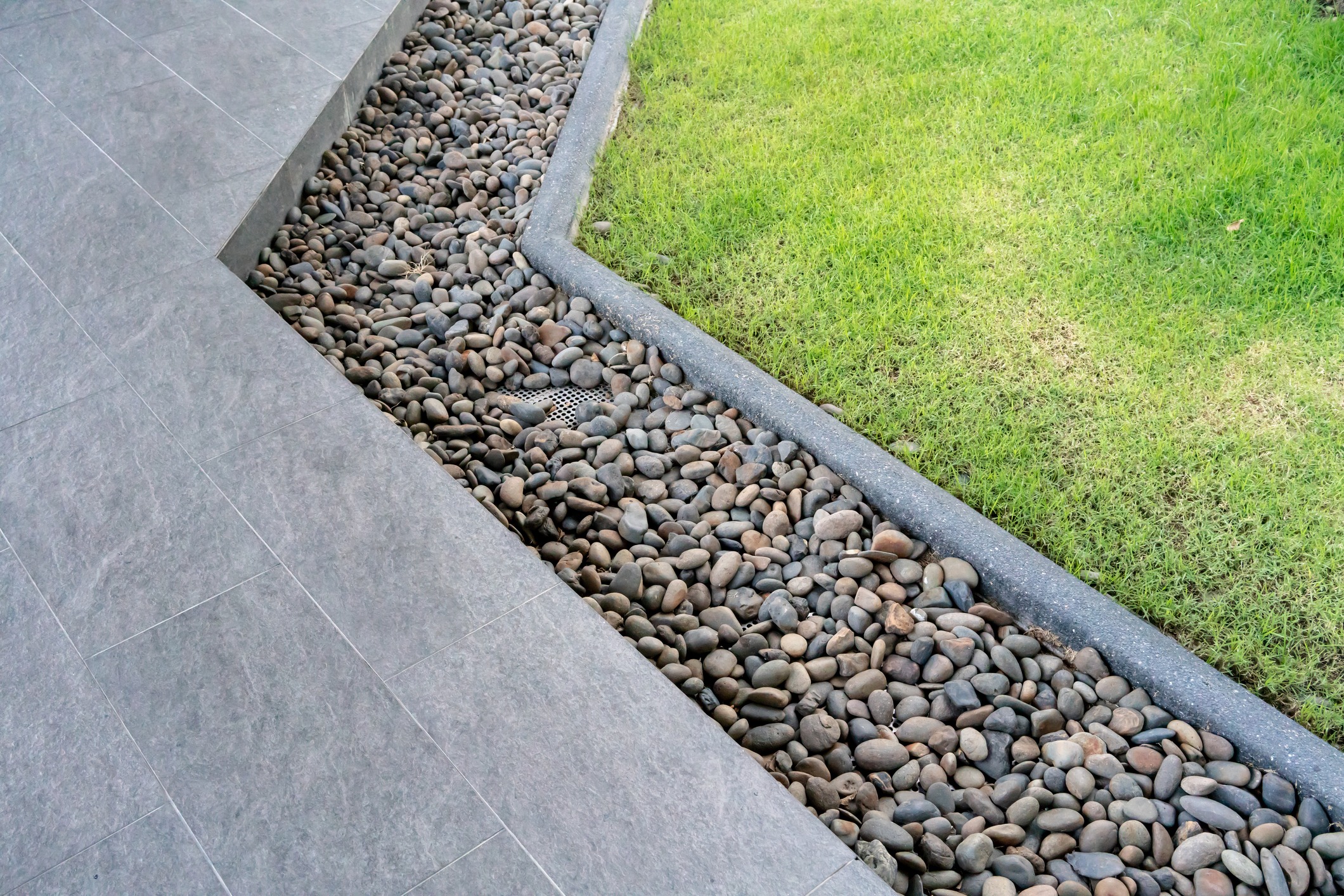 Pebble drainage channel beside gray patio and green lawn
