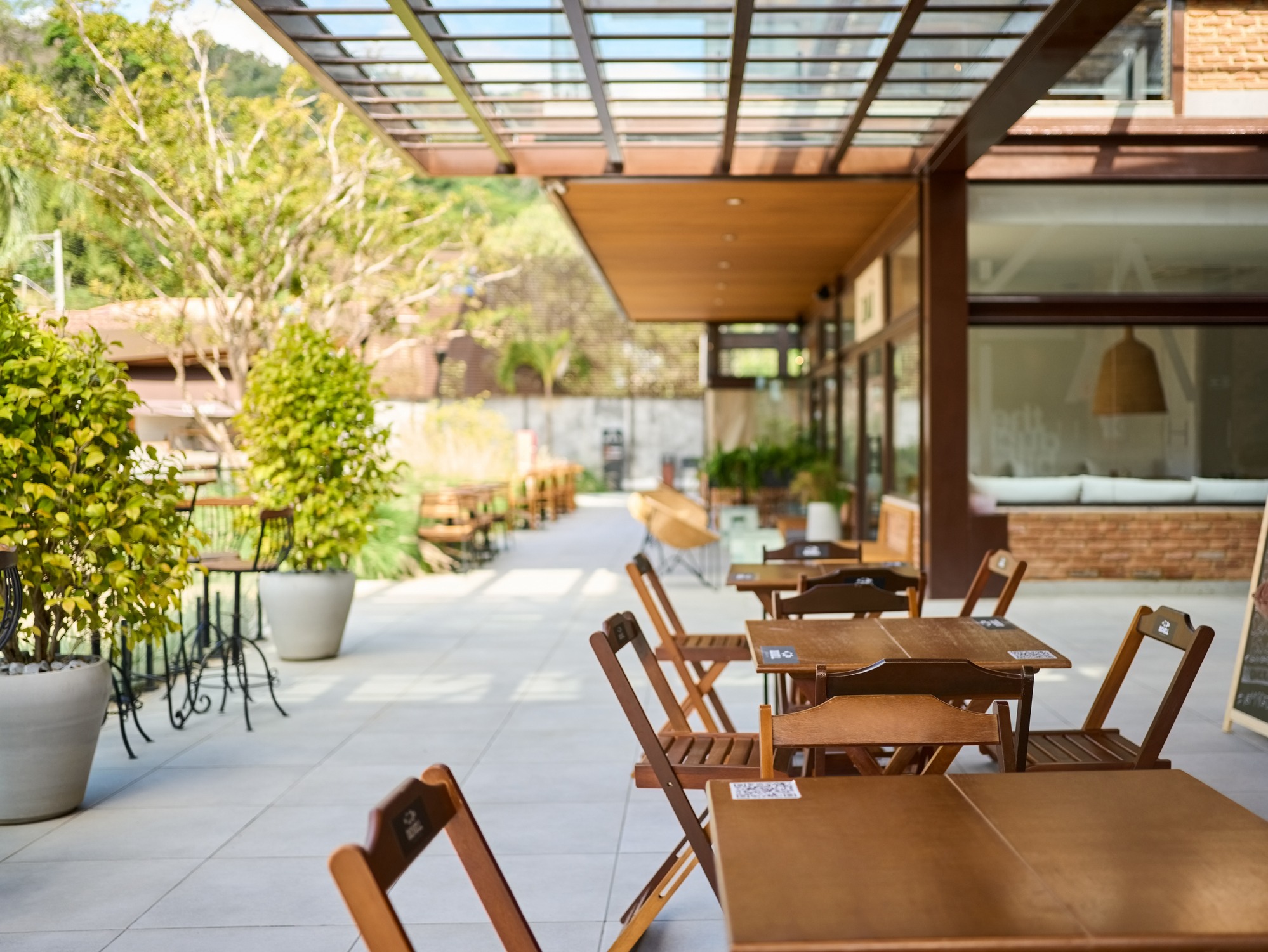 Sunlit outdoor café patio with wooden tables and greenery