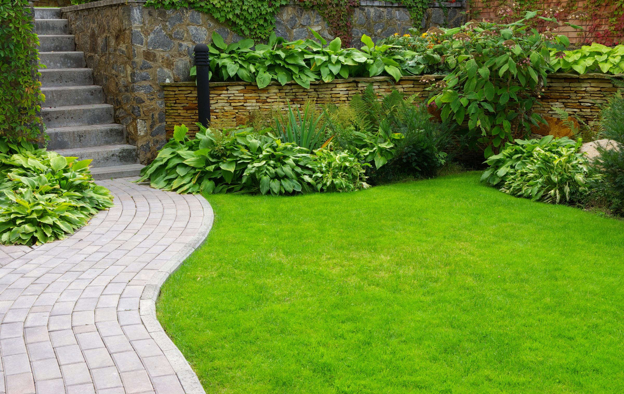 Curved brick path beside lush lawn and stone garden wall