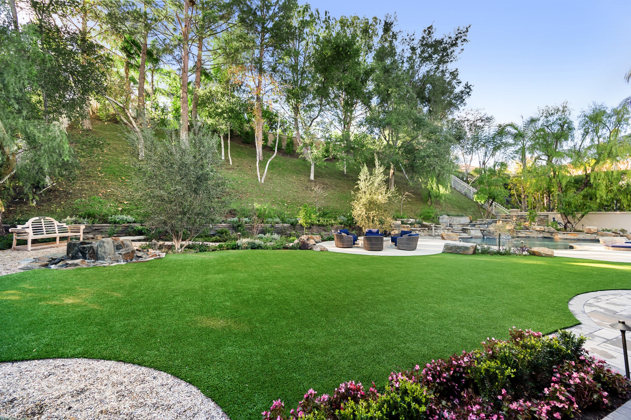 Lush backyard lawn with pool, waterfall, and hillside trees
