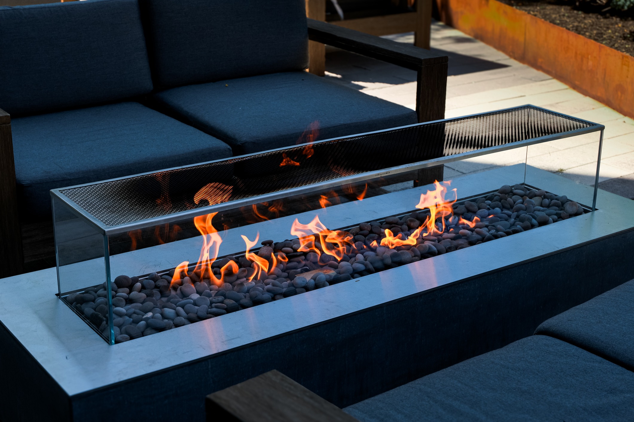 Modern outdoor fire pit beside dark cushioned seating