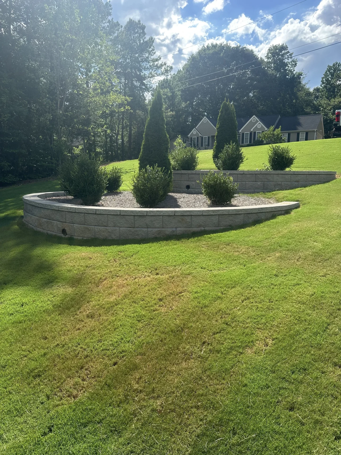 Curved stone retaining wall with landscaped shrubs and evergreens