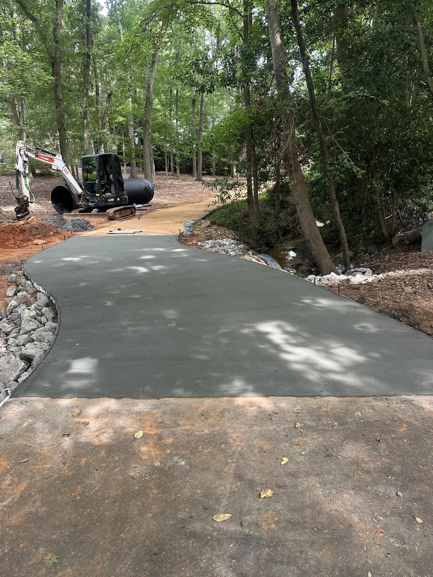Fresh concrete driveway curves through wooded construction site