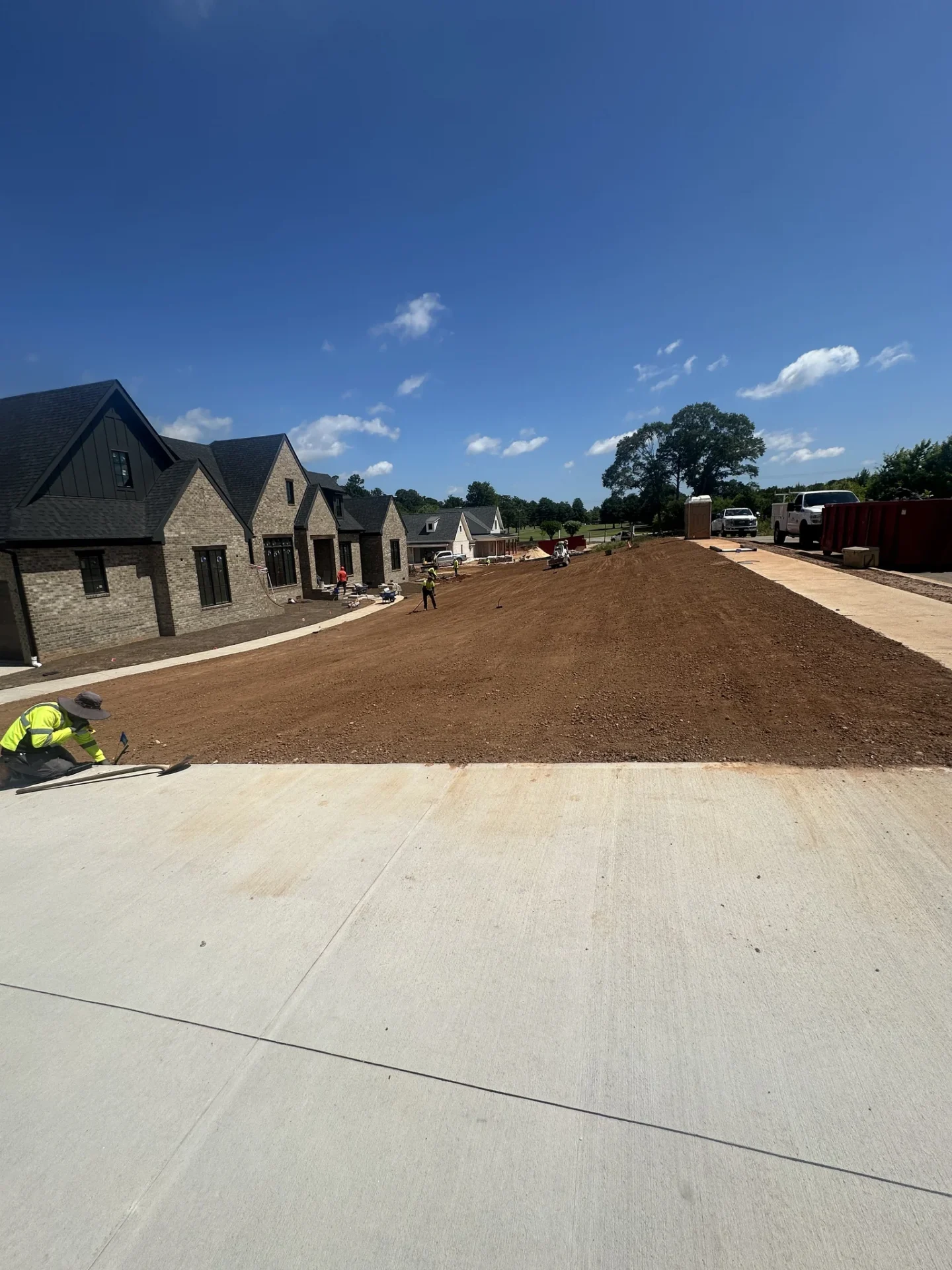 Landscaping crew grades soil beside newly built brick homes.