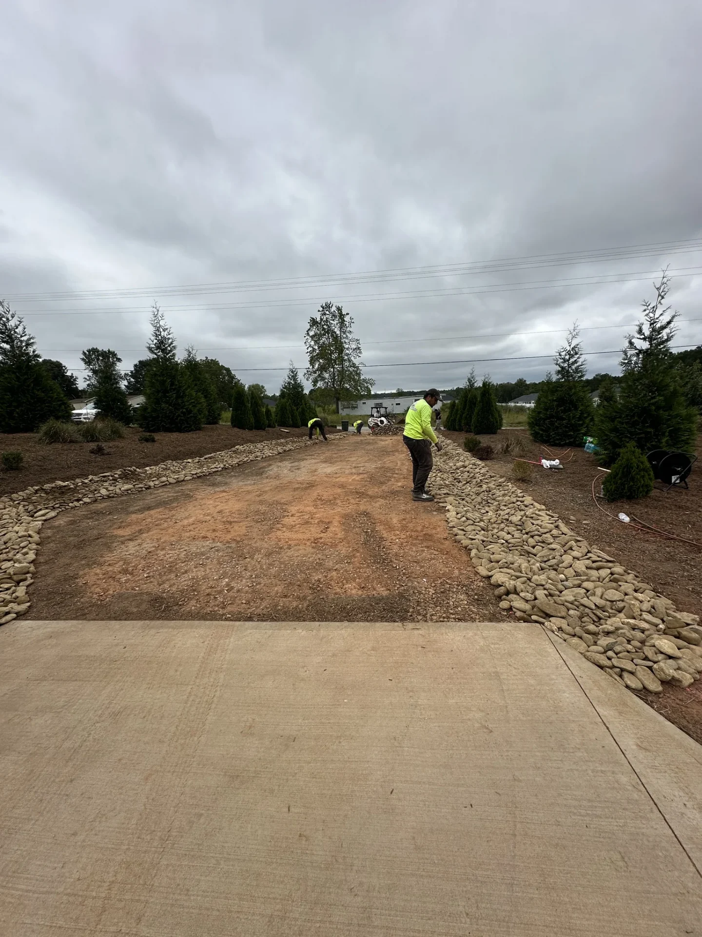 Landscapers install stone borders along a curved dirt driveway.