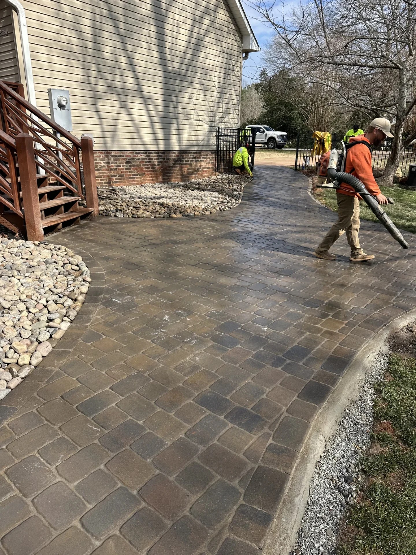 Workers finish a curved paver driveway beside a house.