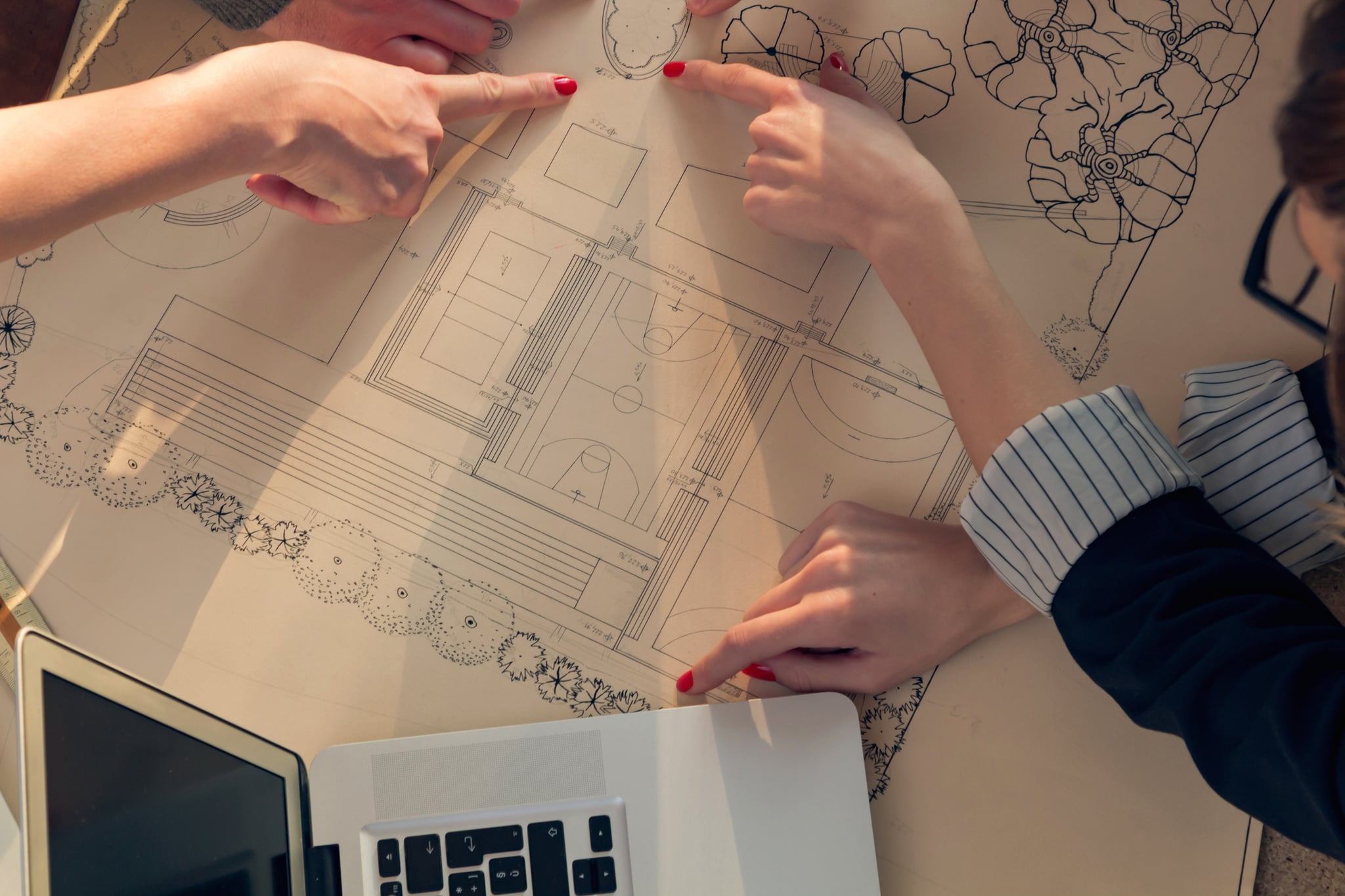 Designers point at architectural blueprints beside a laptop.