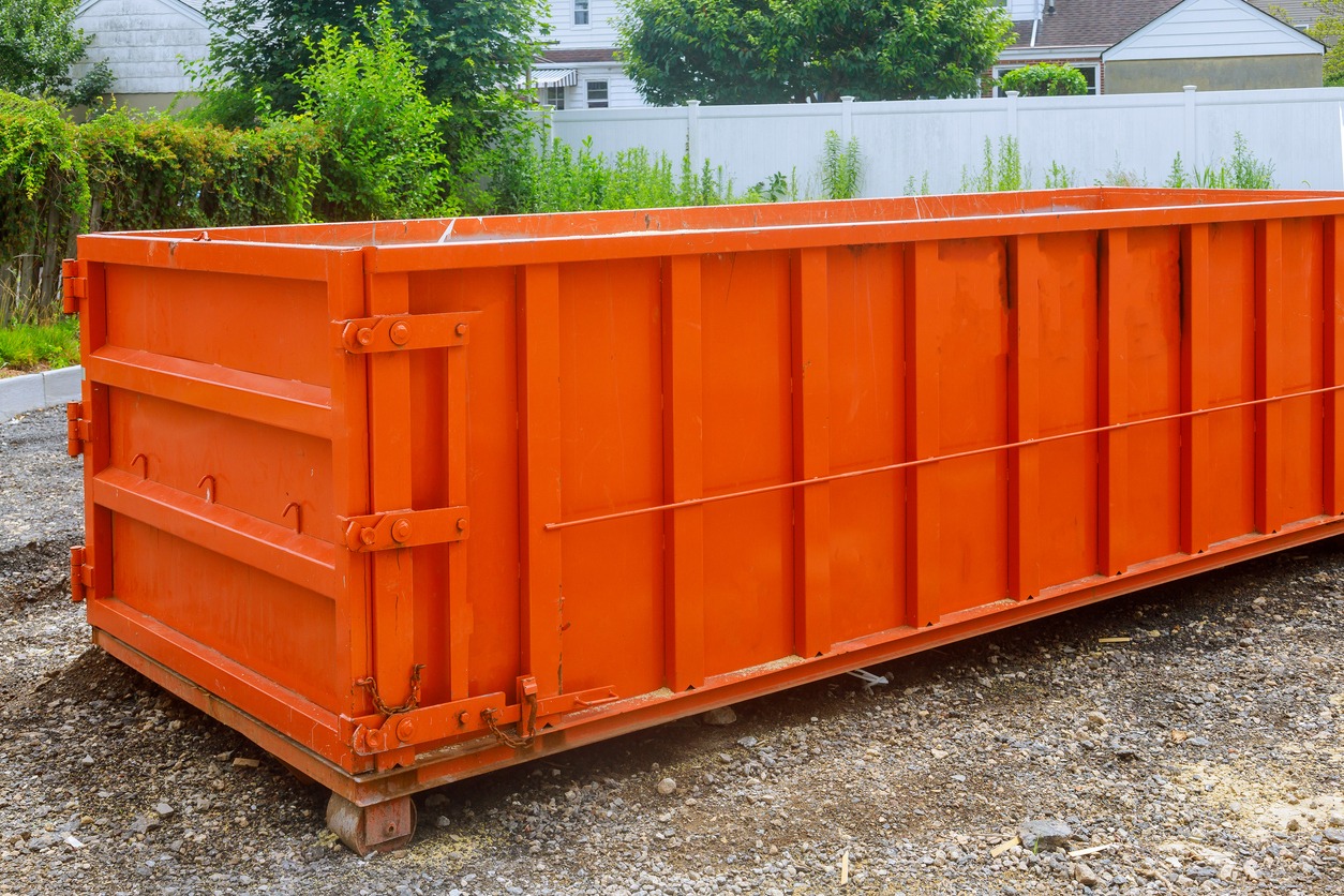 Large orange construction dumpster beside residential homes