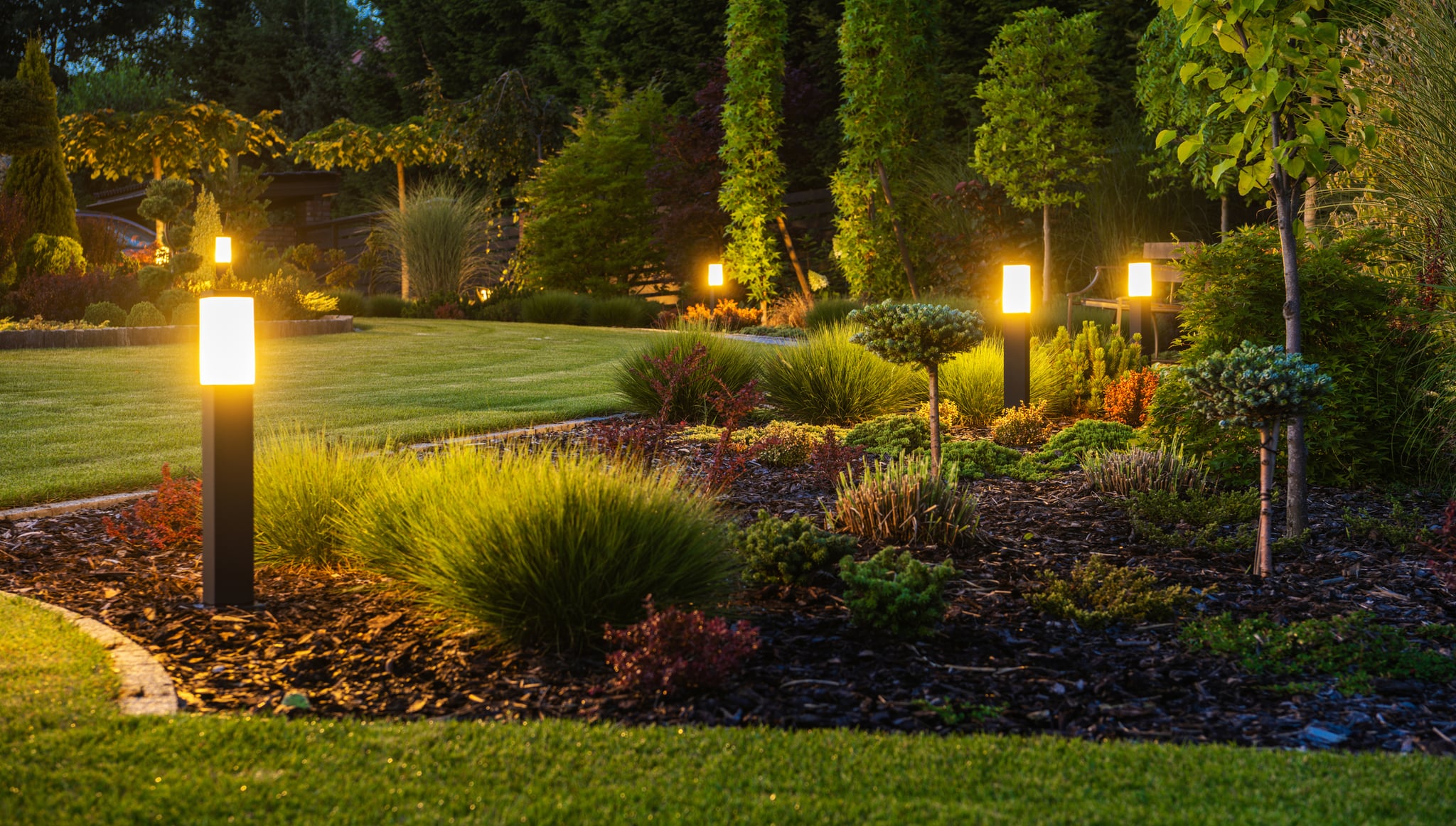 Glowing pathway lights illuminate a landscaped garden at dusk