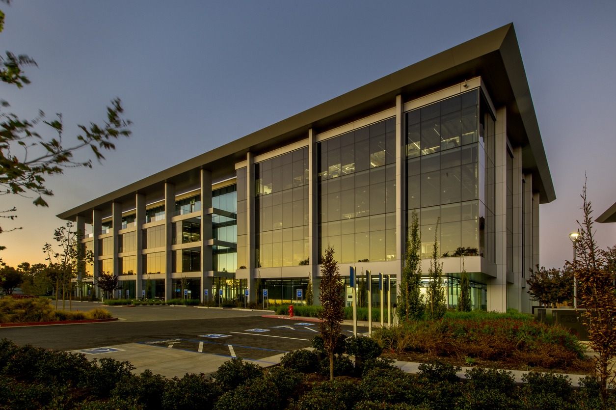Modern glass office building at dusk with landscaped parking lot