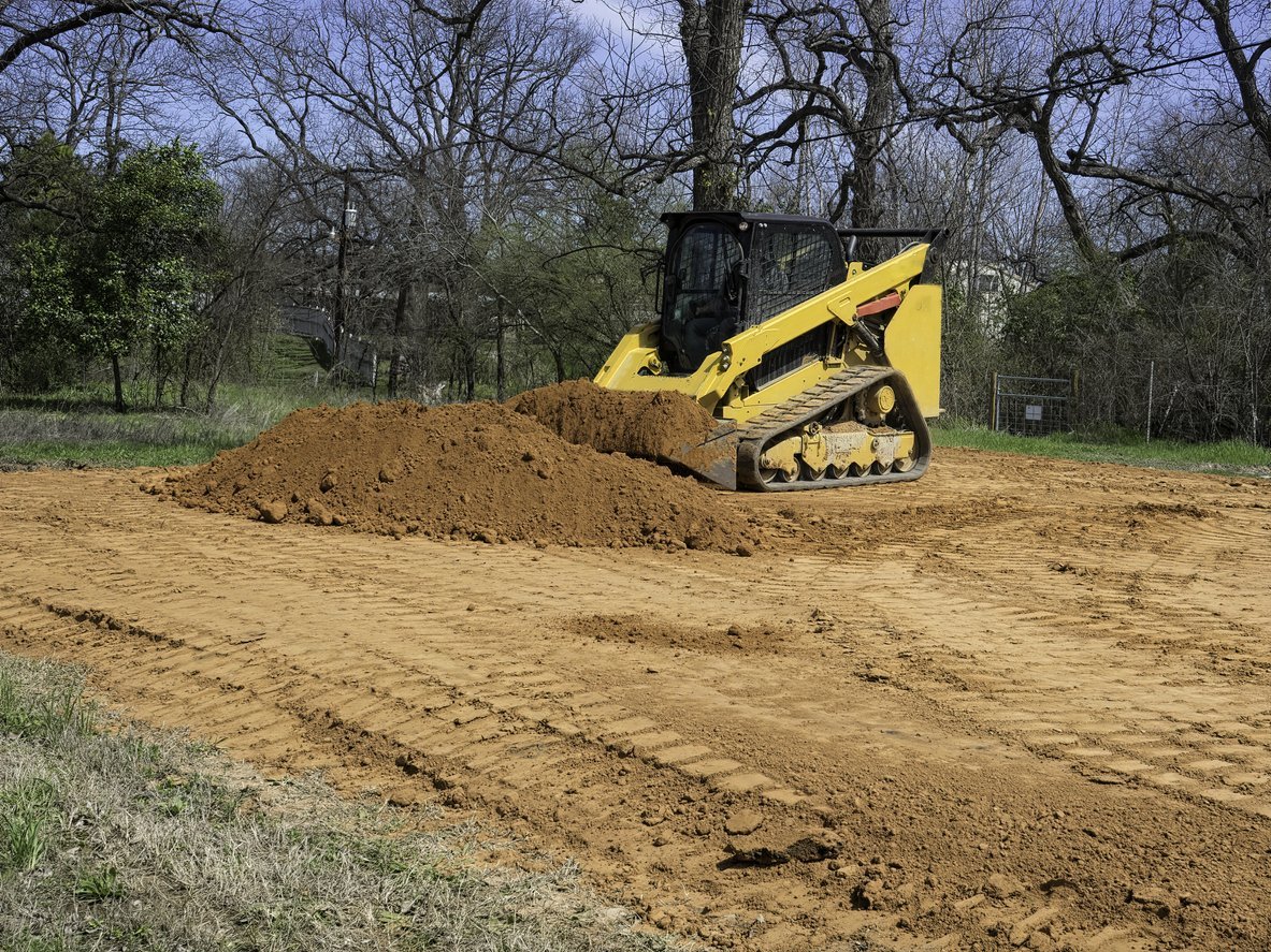 Yellow tracked loader moving dirt at a wooded construction site